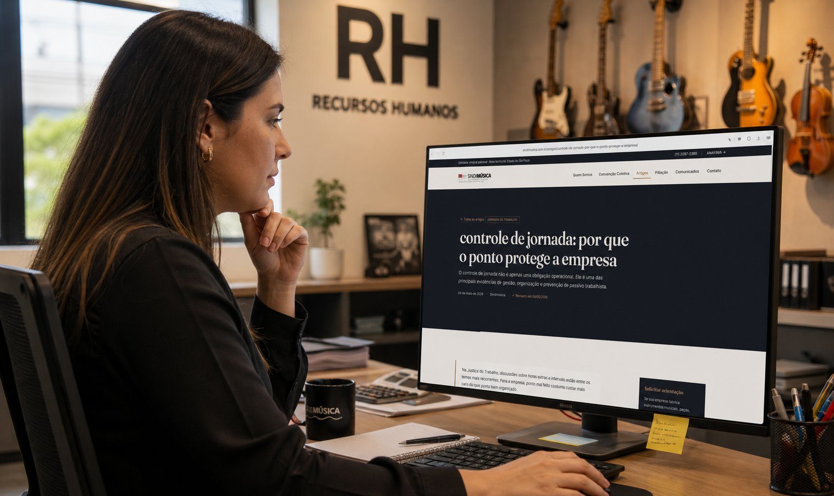 Profissional de RH analisando conteúdo institucional do Sindimúsica em monitor de escritório, com instrumentos musicais ao fundo